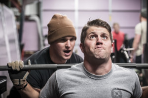 Man lifts weights while friend encourages.